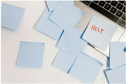 A top-down shot of a laptop keyboard with several light blue sticky notes scattered around it, one of which has the word "HELP" written in orange on it.