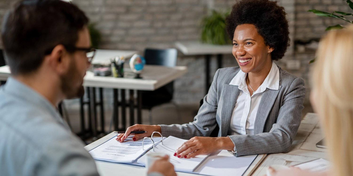 A man and a woman are seated at a table, looking at documents and possibly discussing business or financial matters.