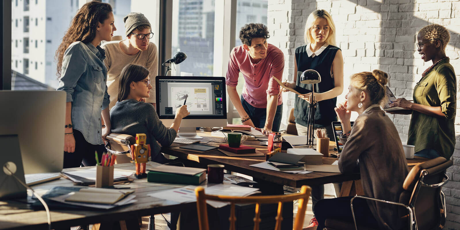 A diverse group of professionals collaborating and brainstorming around a large table in a modern, brightly lit office space.