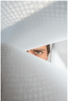 A person's eye peeking through a narrow, angular opening in a light-colored material, possibly paper or fabric.