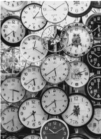 A black and white close-up shot of multiple clock faces, some overlapping, creating a textured pattern. 
